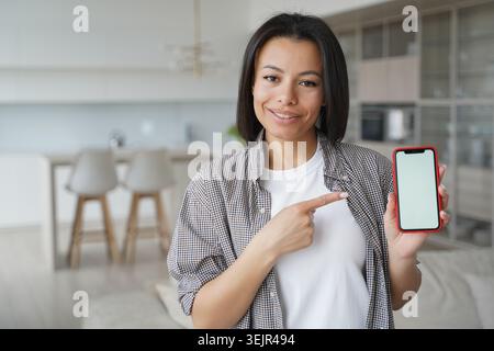 Female customer shows mockup empty phone screen, advertises apps, online service, standing at home Stock Photo