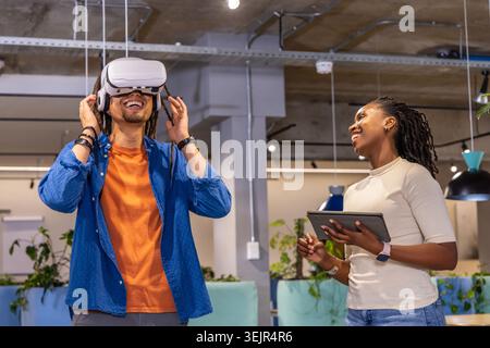 Diverse coworkers testing VR headset with woman holding tablet in open-plan office, copy space. Colleagues, virtual, collaborati Stock Photo
