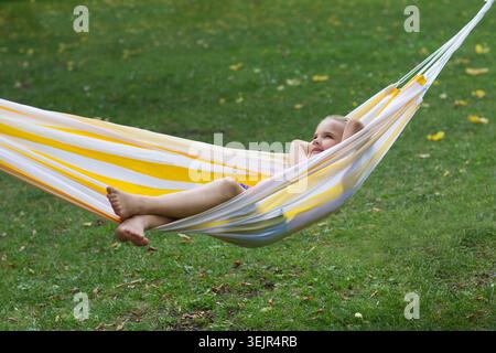 Happy adorable smiling child girl lying in a hammock in summer park. Happy ghild having fun outdoors. Generation Alpha. copy spa Stock Photo
