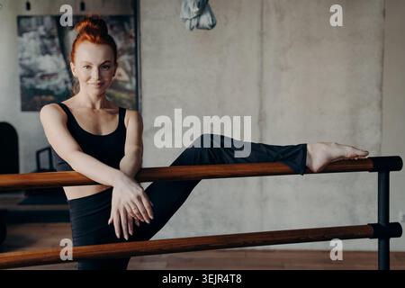 Athletic smiling ginger woman enjoying stretching workout on ballet barre Stock Photo