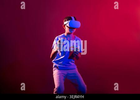 Video Gaming Concept. teenager boy playing with virtual reality goggles, VR headset, modern technology glasses  with neon light Stock Photo