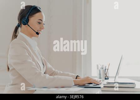 Happy businesswoman in headset talking and using laptop in office Stock Photo