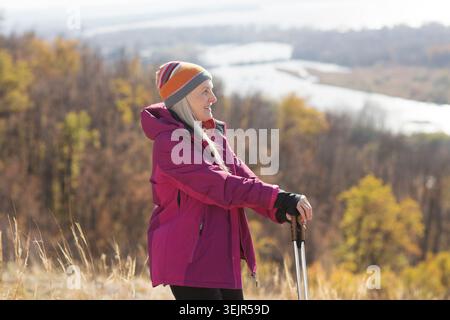 Senior woman  with gray hair  with walking sticks enjoying the autumn landscape standing on the mountain and walks in autumn out Stock Photo