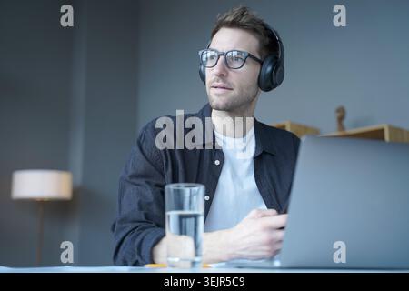 Young european man in wireless headphones listening audio podcast or watching webinar on laptop Stock Photo