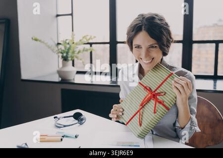 Cheerful lady office employee looking at screen broadly smiling showing to computer camera Xmas gift Stock Photo