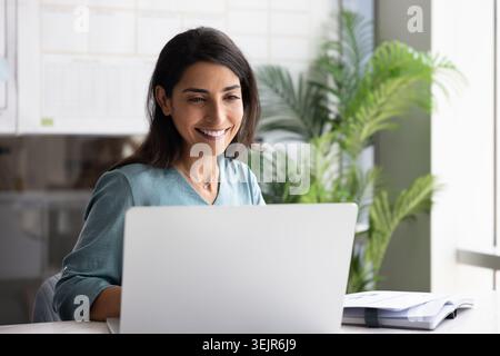 Smiling woman working on laptop in modern office Stock Photo
