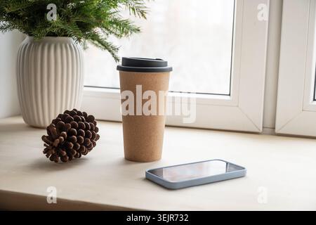 Eco reusable coffee cup and smartphone on windowsill Stock Photo