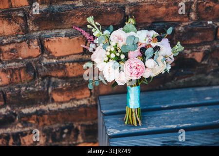 Wedding bouquet with roses and berries on wooden bench against brick wall rustic bridal floral detail Stock Photo