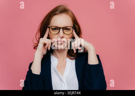 Serious business woman in glasses touching temples isolated on pink background Stock Photo