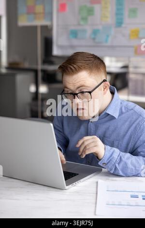 Serious professional man with Down syndrome working on laptop Stock Photo