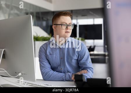 Young man with Down syndrome sitting at desk in office Stock Photo