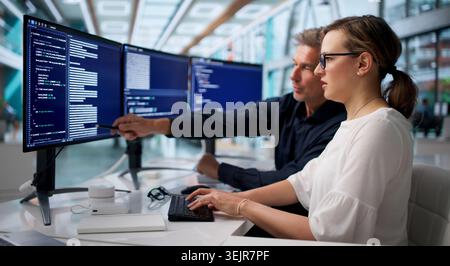 Two Software Engineers Coding Secure Systems Together At Office Desk. Stock Photo
