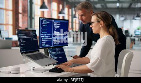 Two Software Engineers Discussing Secure Coding Solutions At Office Desk. Stock Photo