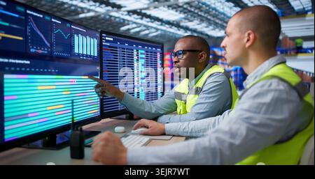 Two Workers Sit In Warehouse Managing Logistics Orders On Computers. Stock Photo