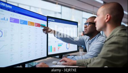 Two Sales Managers Discussing CRM Data On Desktop For Business Growth. Stock Photo
