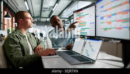 Two Team Members Discuss Project Schedule And Plan Tasks With Laptop Open. Stock Photo