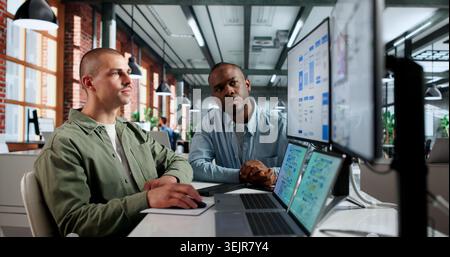 Two Young UX Designers Work Together On App Interface Using Laptops. Stock Photo