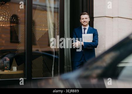 Businessman standing outside office building holding documents and smiling at camera Stock Photo