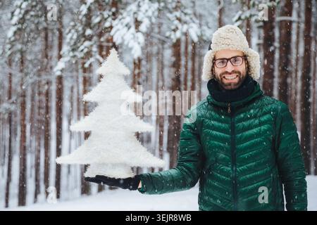 Smiling man holding white Christmas tree decoration in snowy winter forest Stock Photo