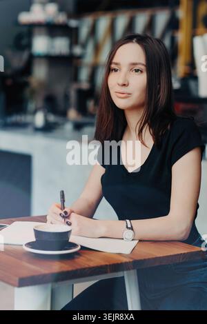 Young woman writing notes at cafe table with coffee cup and notebook Stock Photo