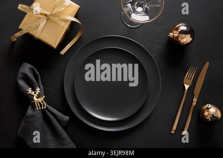 Christmas table setting with black plate and golden decorations on black. Stock Photo