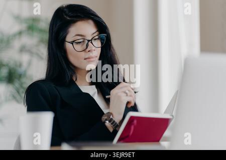 Business woman taking notes while working on laptop at office desk Stock Photo