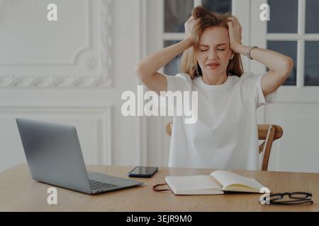 Stressed woman working on laptop at home feeling overwhelmed and frustrated Stock Photo