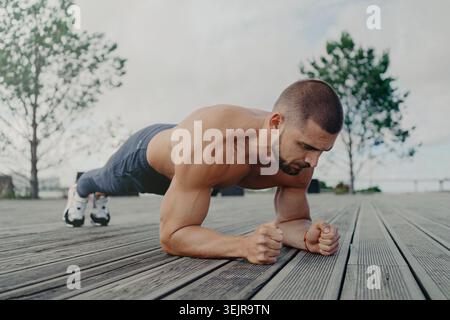 Athletic man doing plank exercise outdoors on wooden deck Stock Photo