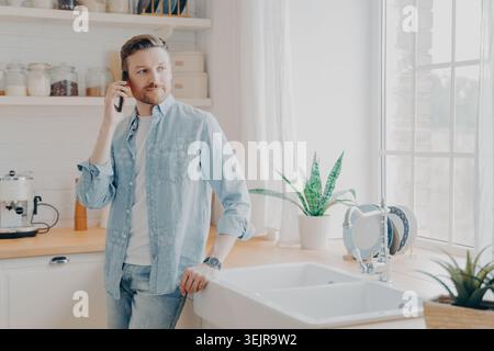 Man talking on smartphone in bright kitchen at home Stock Photo
