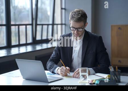 Business man working on laptop and writing notes at office desk Stock Photo