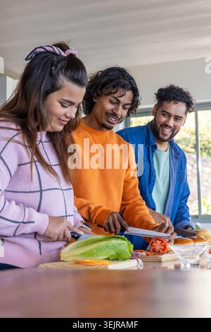 Diverse friends chopping lettuce and slicing tomato at kitchen counter using knives and boards. Cooking, group, trio, multicultu Stock Photo
