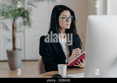 Business woman taking notes while working at computer in modern office Stock Photo