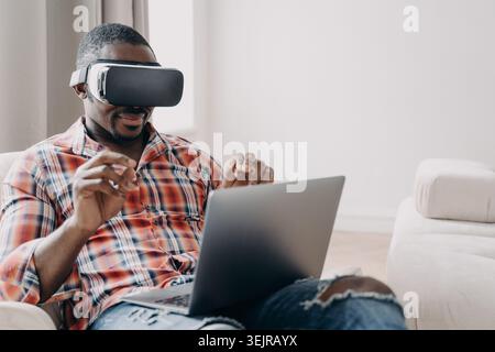 Black man using virtual reality headset with laptop at home Stock Photo