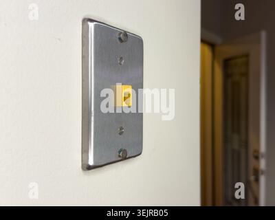 A light switch plate is mounted on a white wall. The switch has a yellow insert and is located near an open doorway leading to another room. Stock Photo