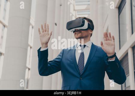 Businessman Using Virtual Reality Headset in Modern Office Building Raising Hands During VR Experience Stock Photo