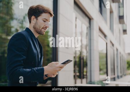 Professional Man Using Smartphone Outside Modern Office Building Checking Messages Stock Photo