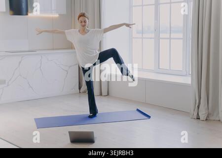 Young Woman Doing Online Ballet Exercise at Home on Mat Following Laptop Dance Class Stock Photo