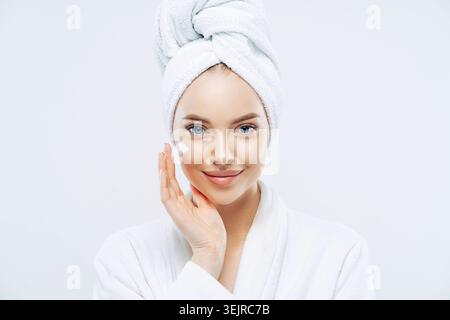 Young Woman Applying Face Cream Wearing White Bathrobe and Towel During Skincare Routine Stock Photo