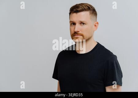 Serious Young Man Portrait Wearing Black T Shirt Against Clean Gray Studio Background Stock Photo