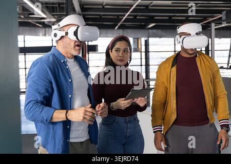 Diverse coworkers testing virtual reality headsets at modern open-plan office, woman holding tablet. Vr, collaboration, teamwork Stock Photo
