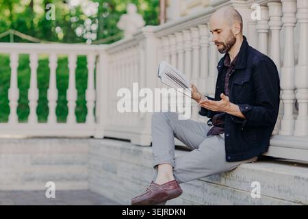 Focused Adult Man Reading Paper Documents While Sitting on Outdoor Stone Steps Near White Railing in Quiet Park Setting Stock Photo