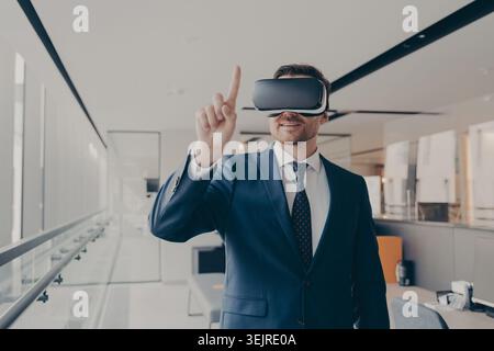 Confident business man wearing virtual reality headset in modern office touching interface during immersive technology presentat Stock Photo