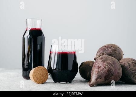 Beetroot juice in glass and bottle with fresh beets on light kitchen surface Stock Photo