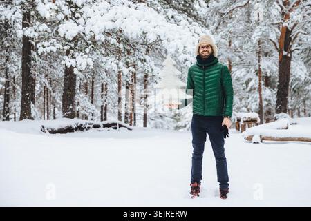 Smiling man holds a small snow covered tree while standing in a winter forest Stock Photo