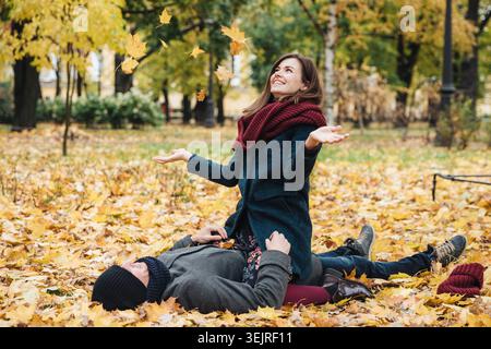 Young couple plays with fallen autumn leaves while relaxing together in city park Stock Photo