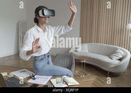 Young woman uses virtual reality headset while working at home office in modern living room Stock Photo