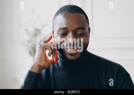 Smiling Black man talking on smartphone during business call in bright modern interior Stock Photo