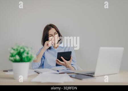 Businesswoman using calculator with laptop and paperwork at office desk Stock Photo