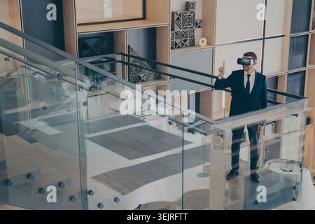 Businessman using virtual reality headset in modern office stairwell Stock Photo