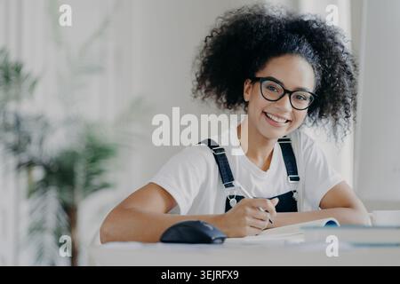 Black young woman studying with notebook and books at home desk Stock Photo